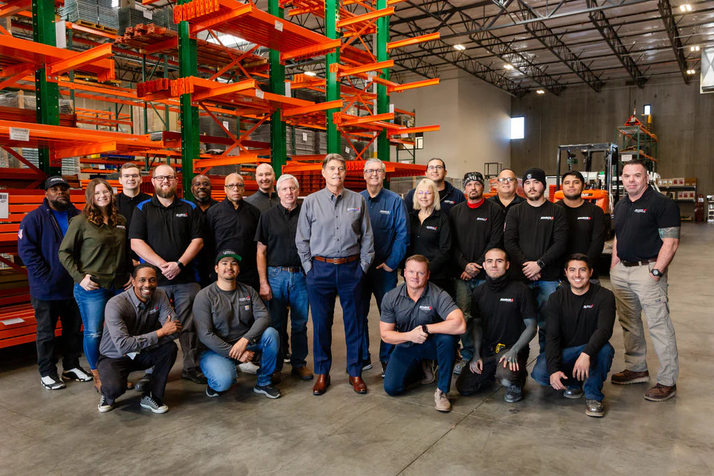 Source 4 Industries team standing in warehouse with orange racks, representing personal service and client-focused support.