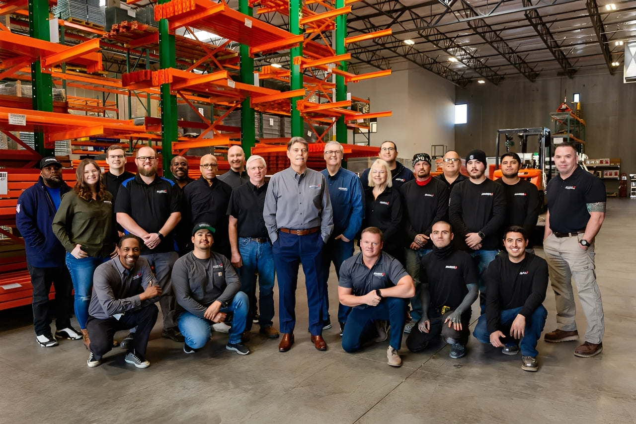 Source 4 Industries team standing in warehouse with orange racks, representing personal service and client-focused support.